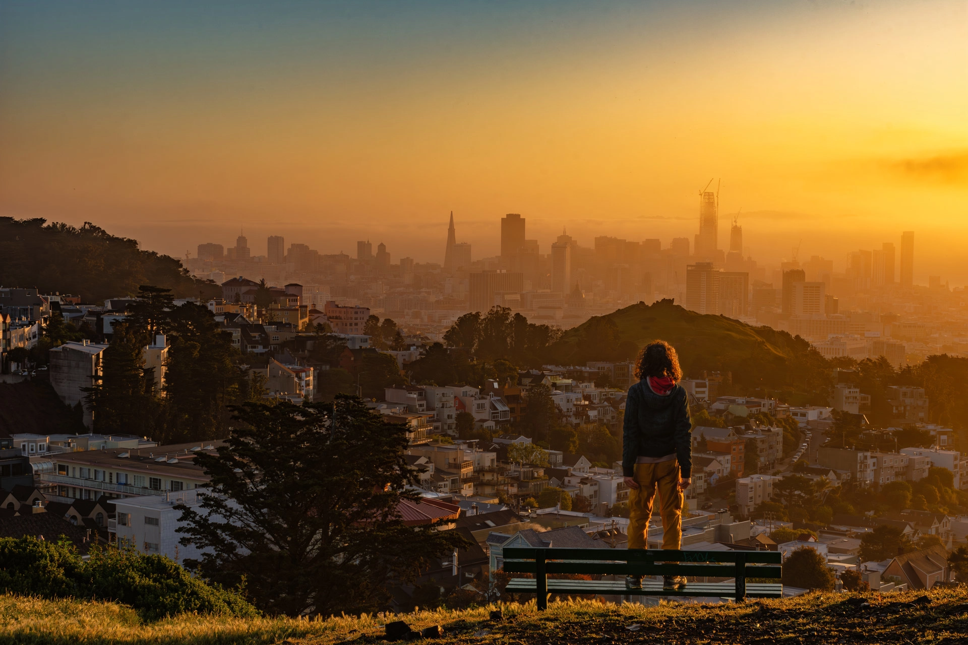 back of male figure overlooking San Francisco from hilltop at sunrise