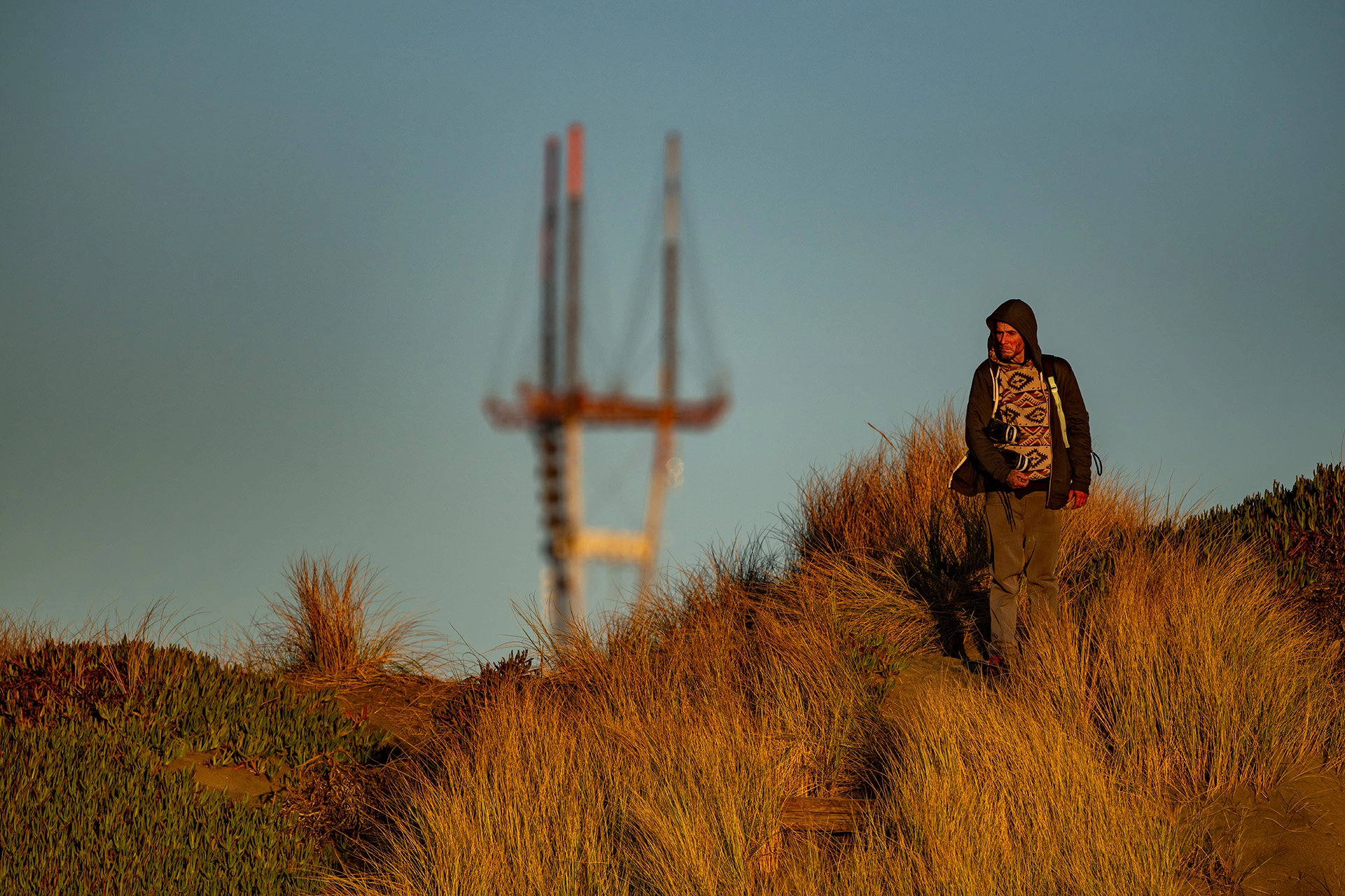 man in poncho on ocean dunes at sunset in front of sutro tower